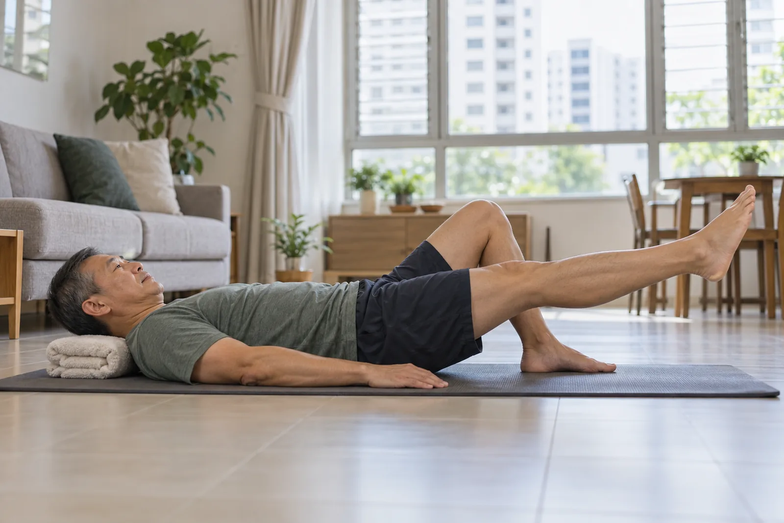 A man performs a controlled straight-leg raise on an exercise mat in a bright living room.
