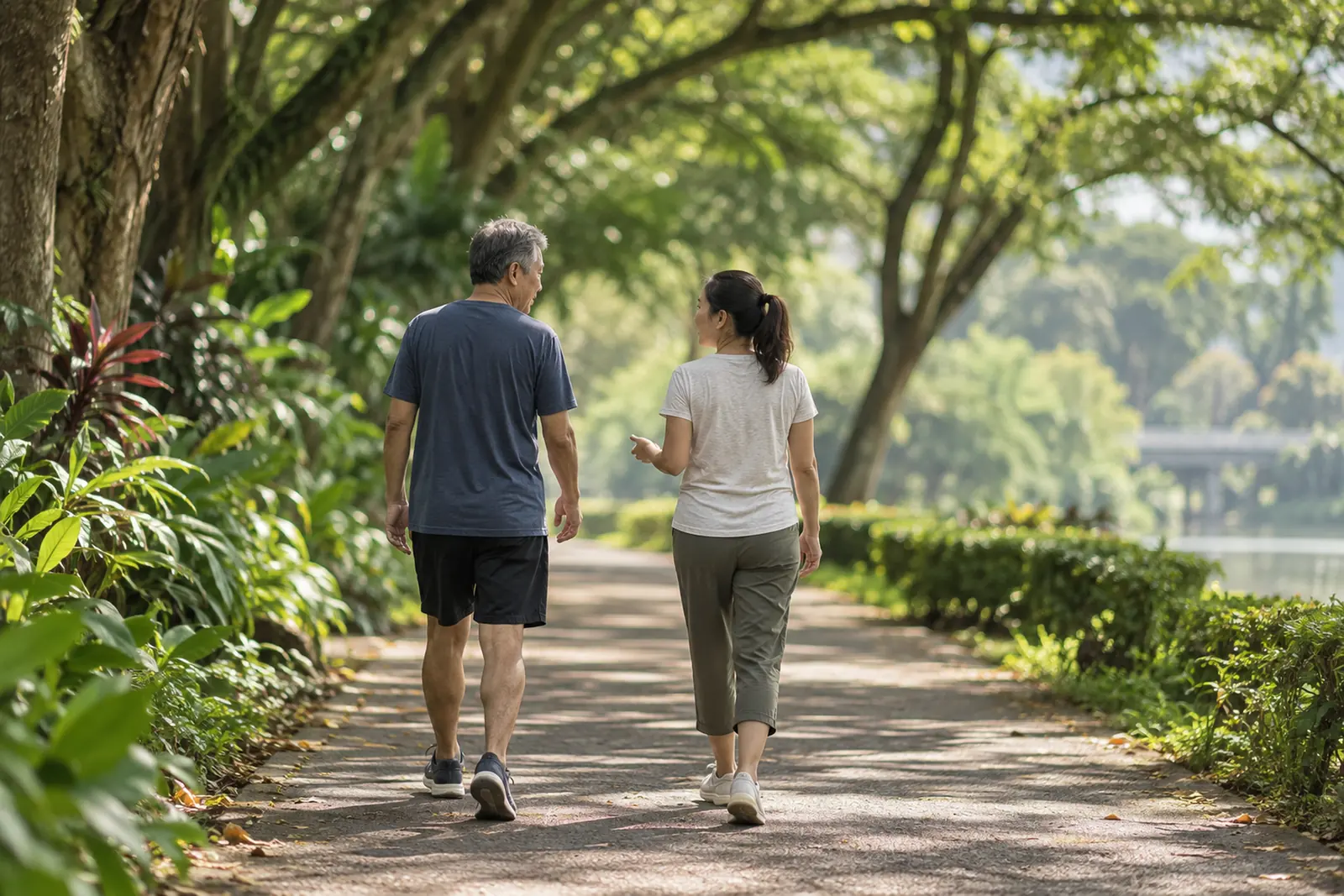Two adults walk side by side in quiet conversation along a shaded park connector.