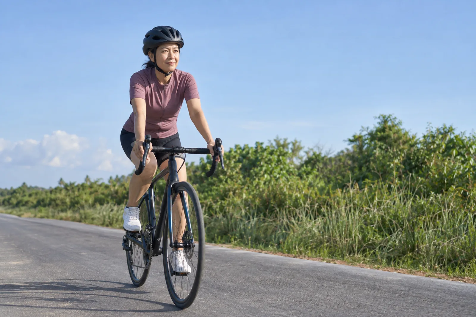 A woman rides a road bicycle at an easy pace along a quiet country road.