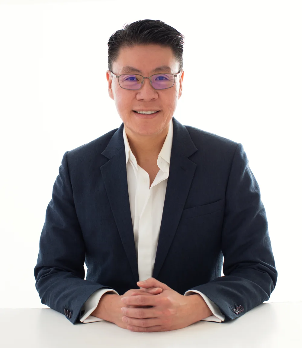 Dr Sean Leo seated at a desk in a jacket, hands folded