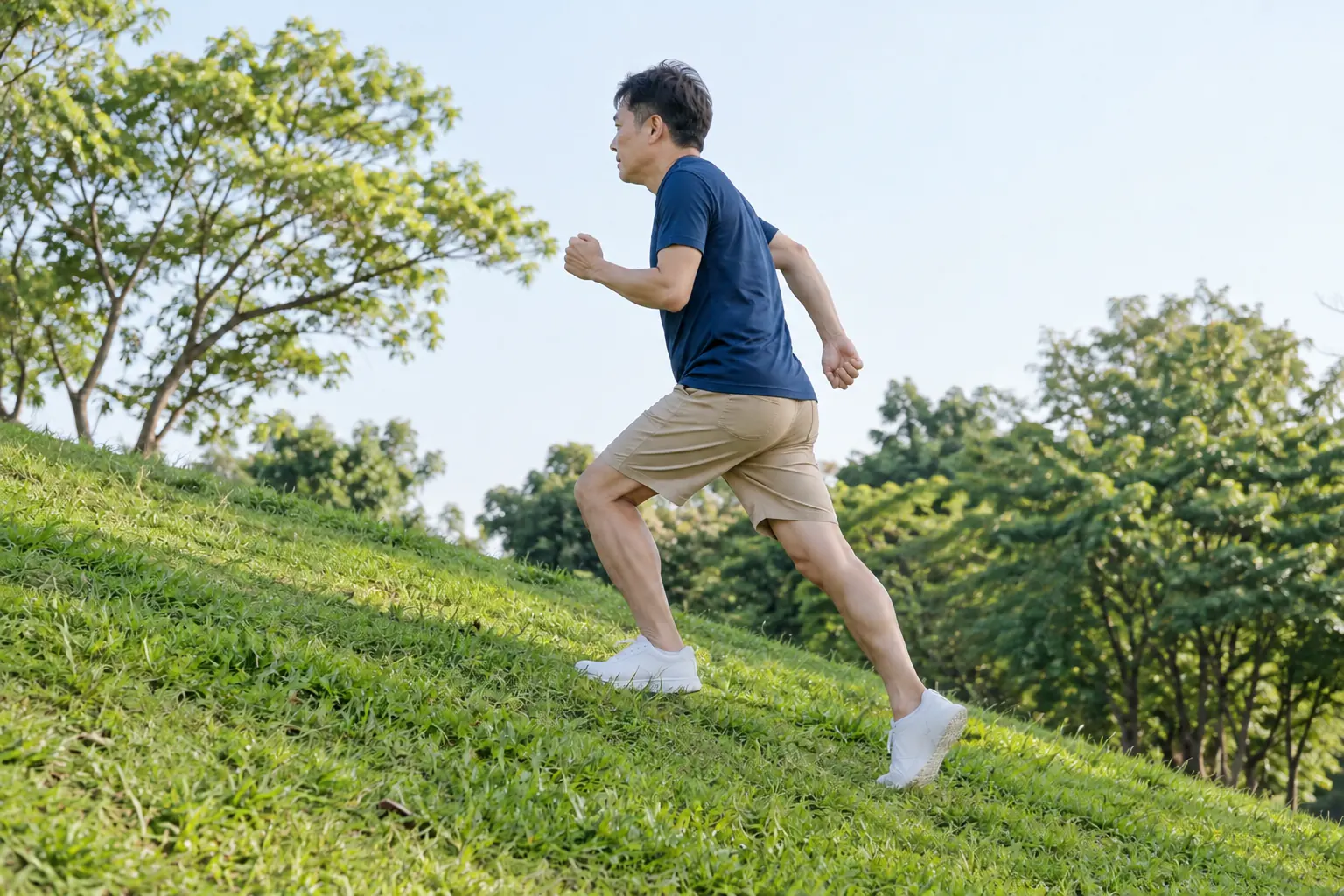A man runs up a grassy slope in a park, with the backs of his lower legs and heels visible.