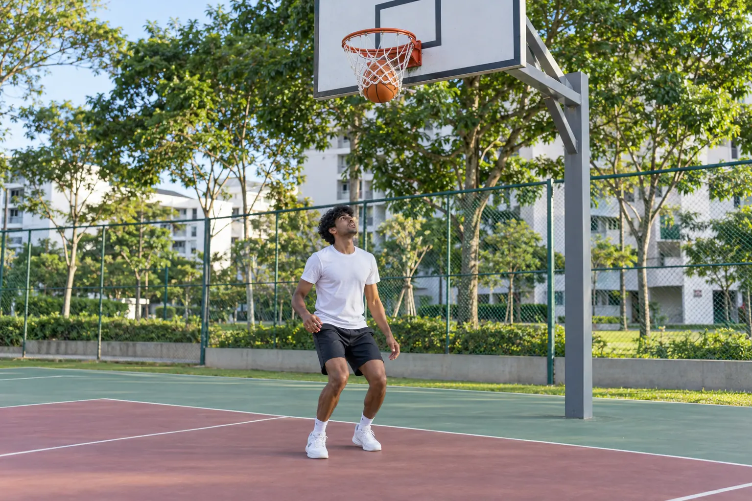 A young man lands with bent knees beneath a basketball hoop as the ball drops through the net.