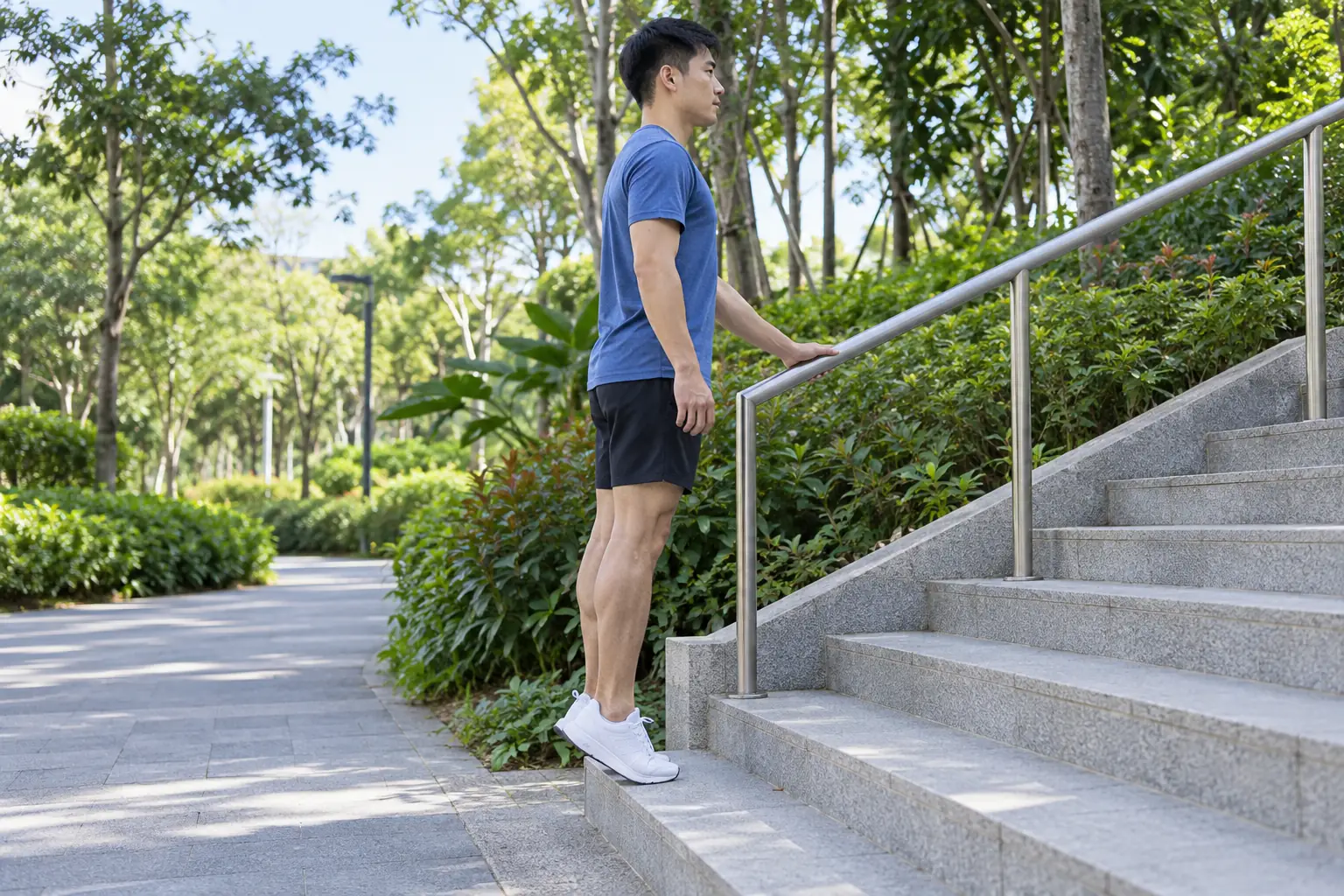 A man raises his heels on the bottom park step with one hand resting on a rail.