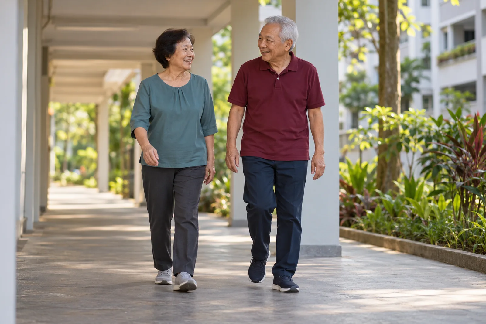 An older couple walk side by side and chat along a covered walkway between housing blocks.