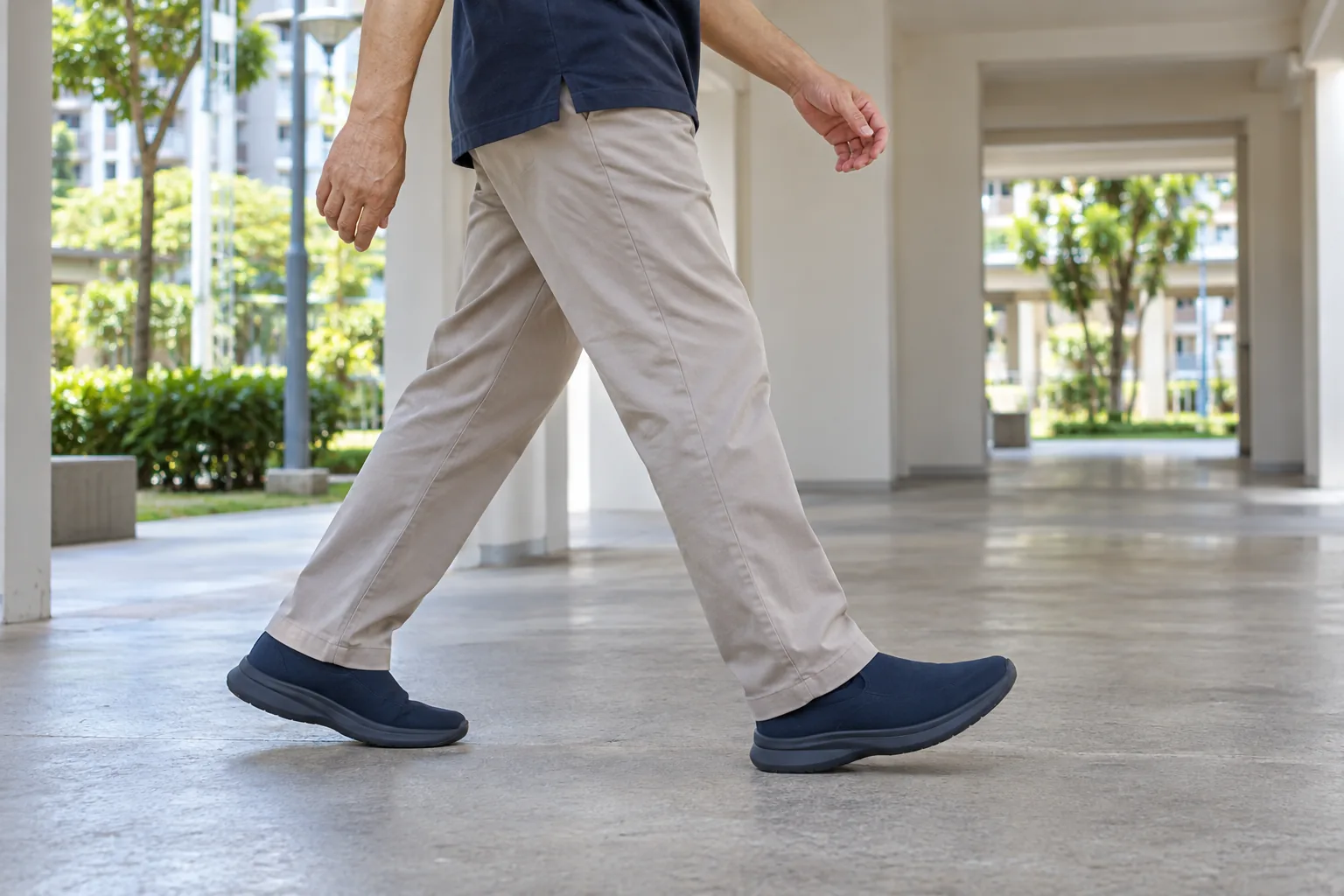 A man walks through a covered housing-block walkway wearing plain navy shoes with broad low heels.