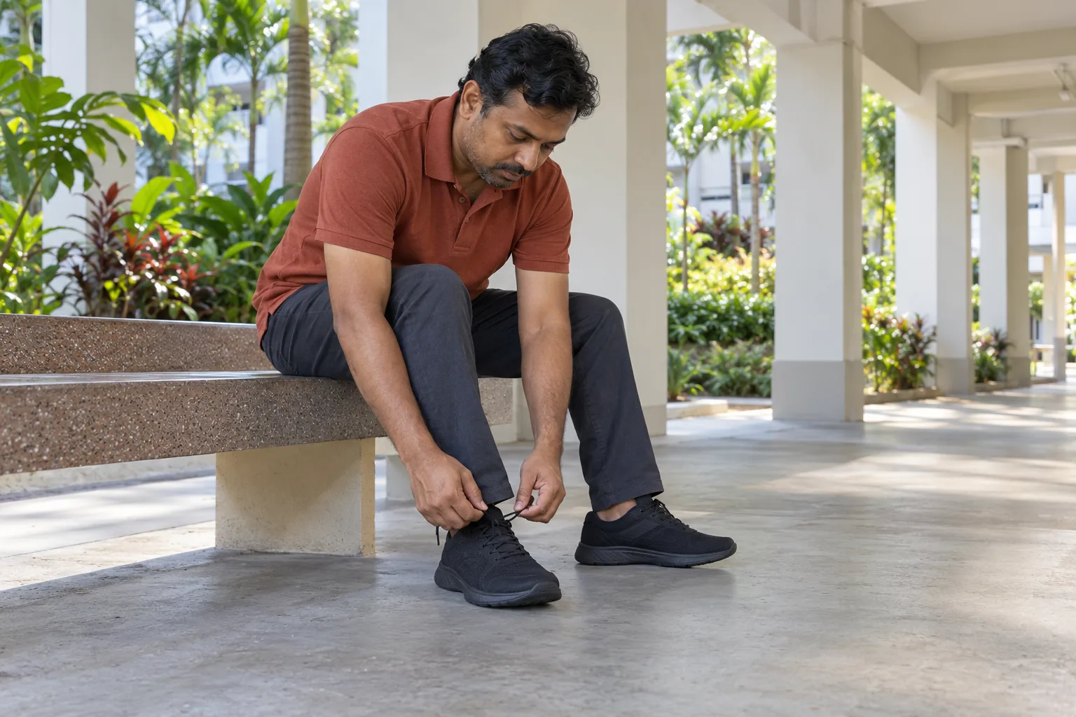 An Indian Singaporean man ties his walking shoes on a void-deck bench.