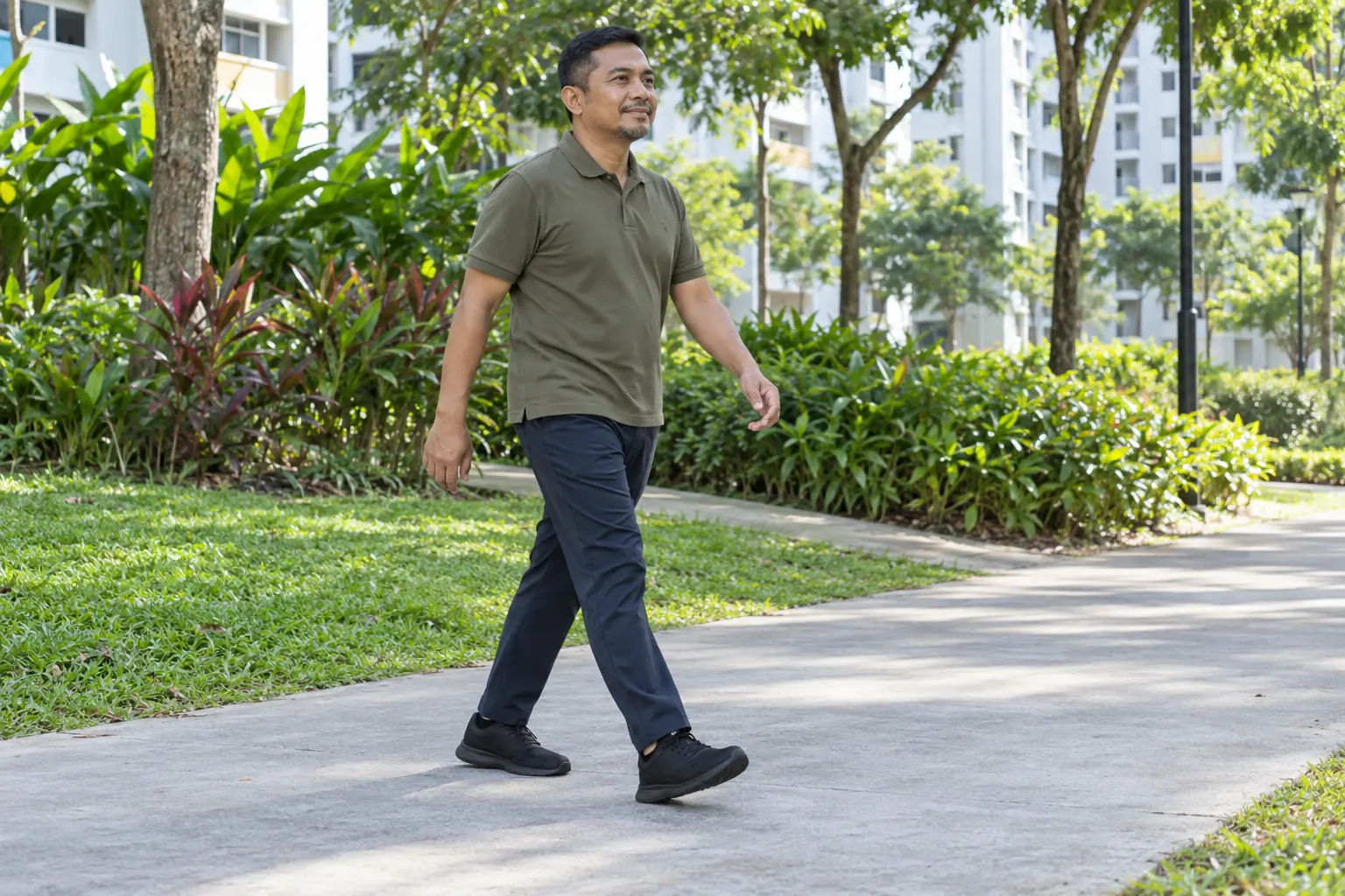 A Malay man walks along a flat park path in plain walking shoes.
