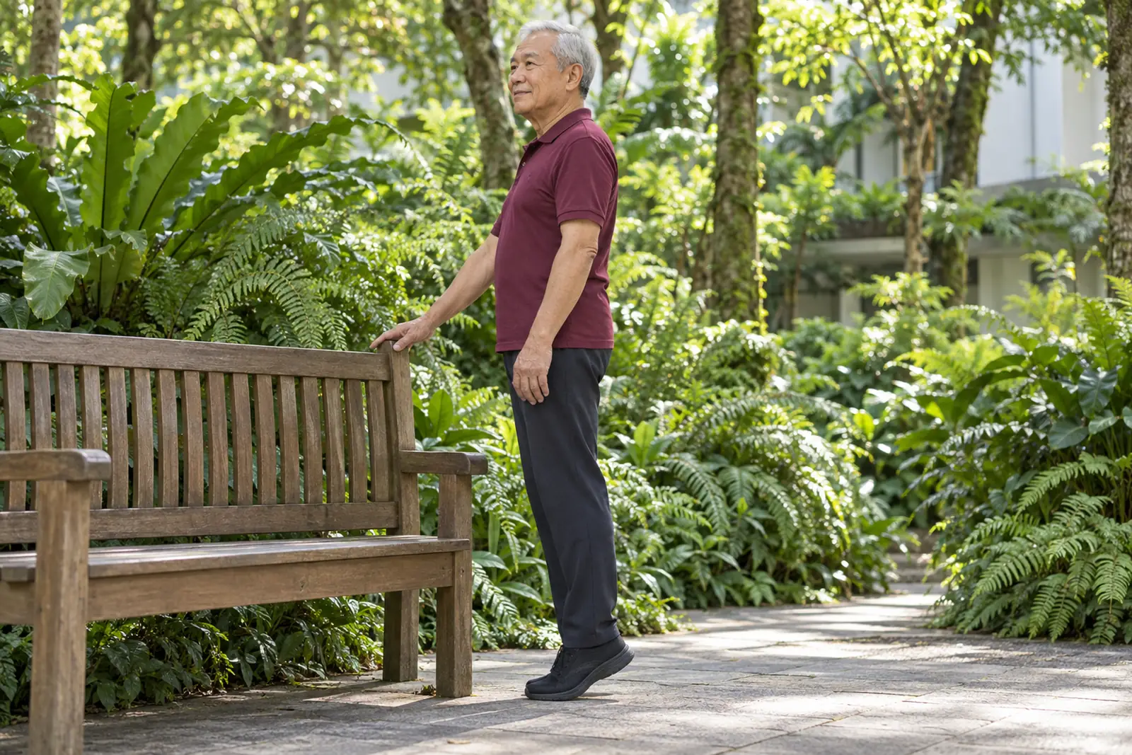 An older man practises a slow balance exercise beside a timber bench in a shady fern garden.