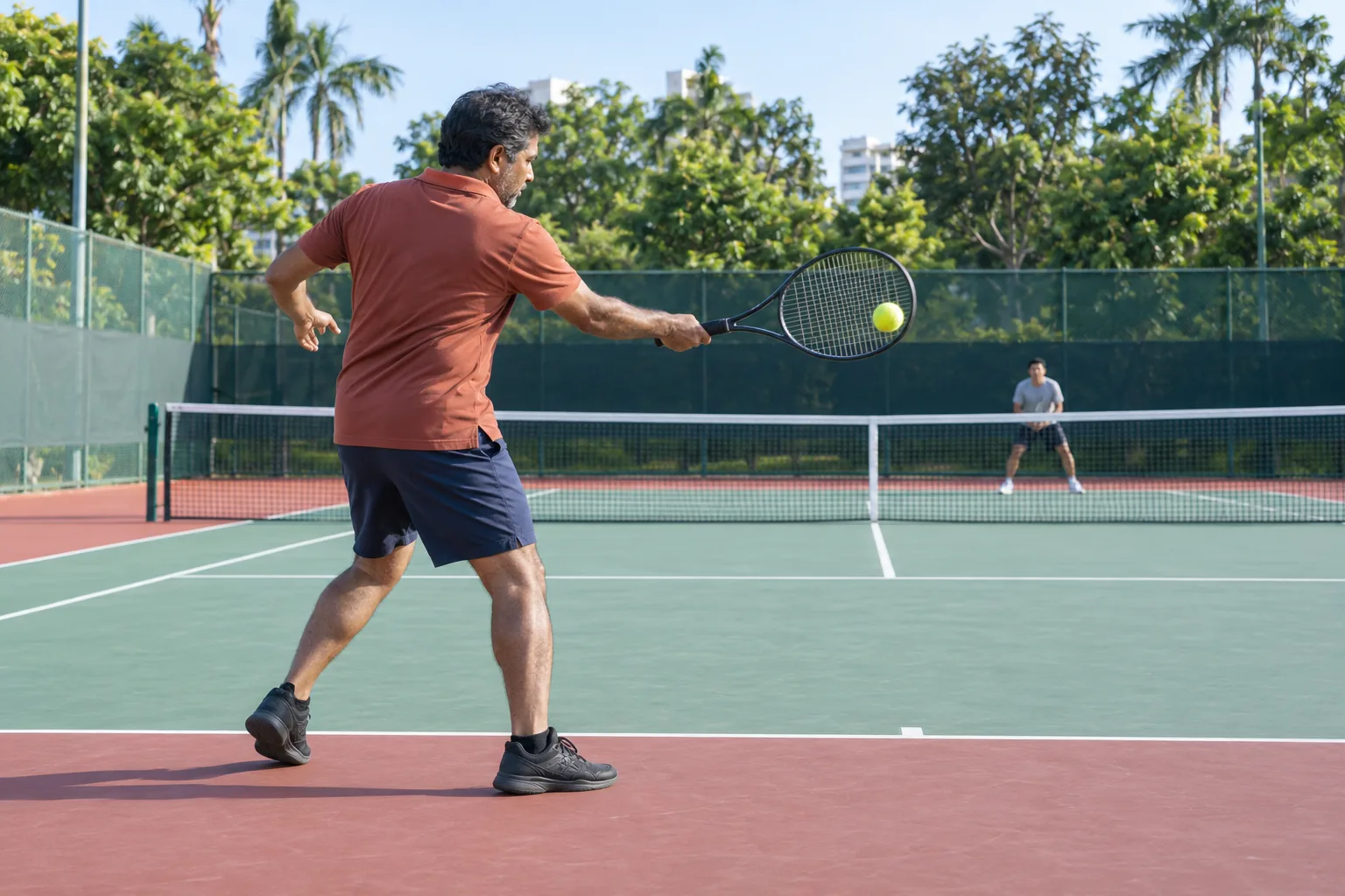 An Indian man hits a forehand from the baseline of a public tennis court.