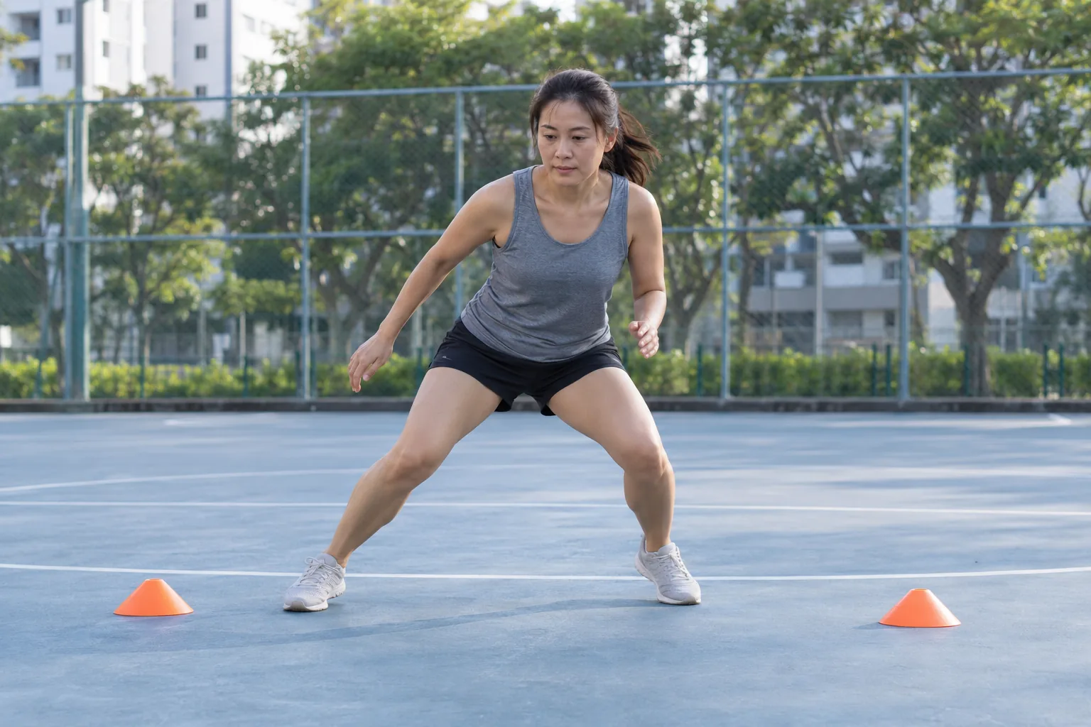 A woman performs a low side-to-side shuffle between two cones with bent knees and her weight over the outside leg.