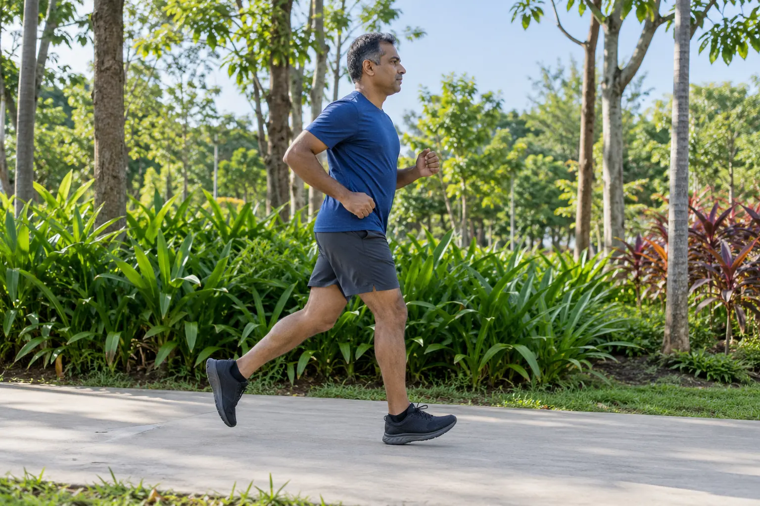 A man jogs along a tree-lined park path with one knee taking his weight.