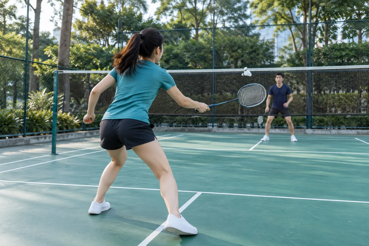 A woman pivots during badminton while facing the net and the shuttle in front of her.