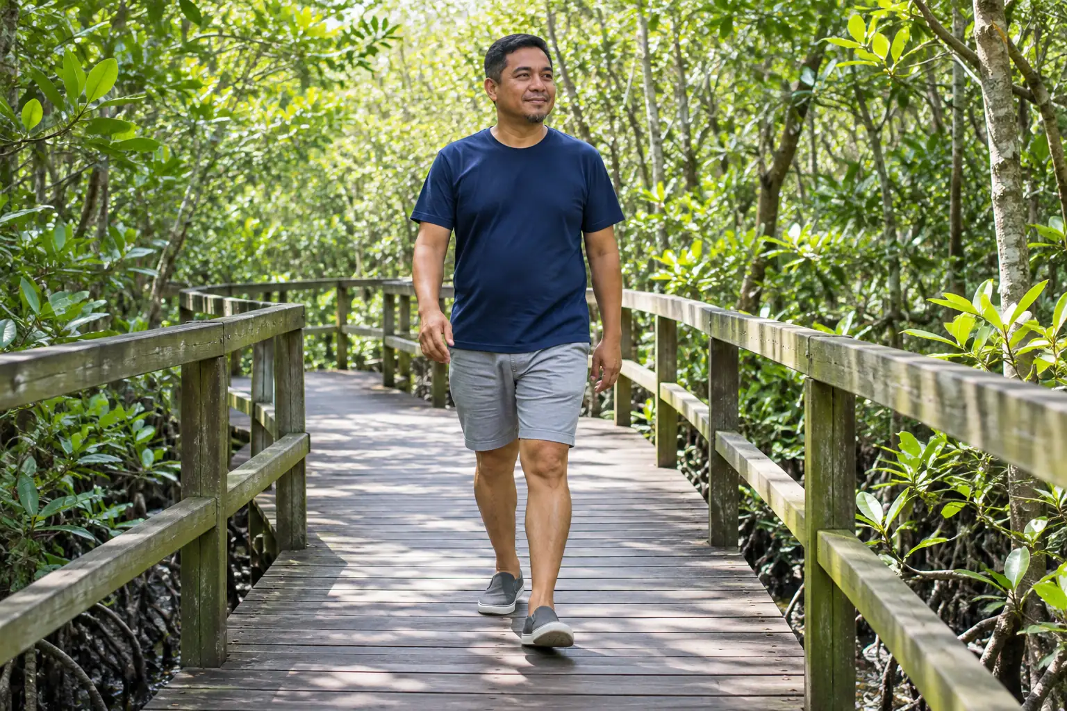 A man walks at an easy pace along a boardwalk through mangroves.