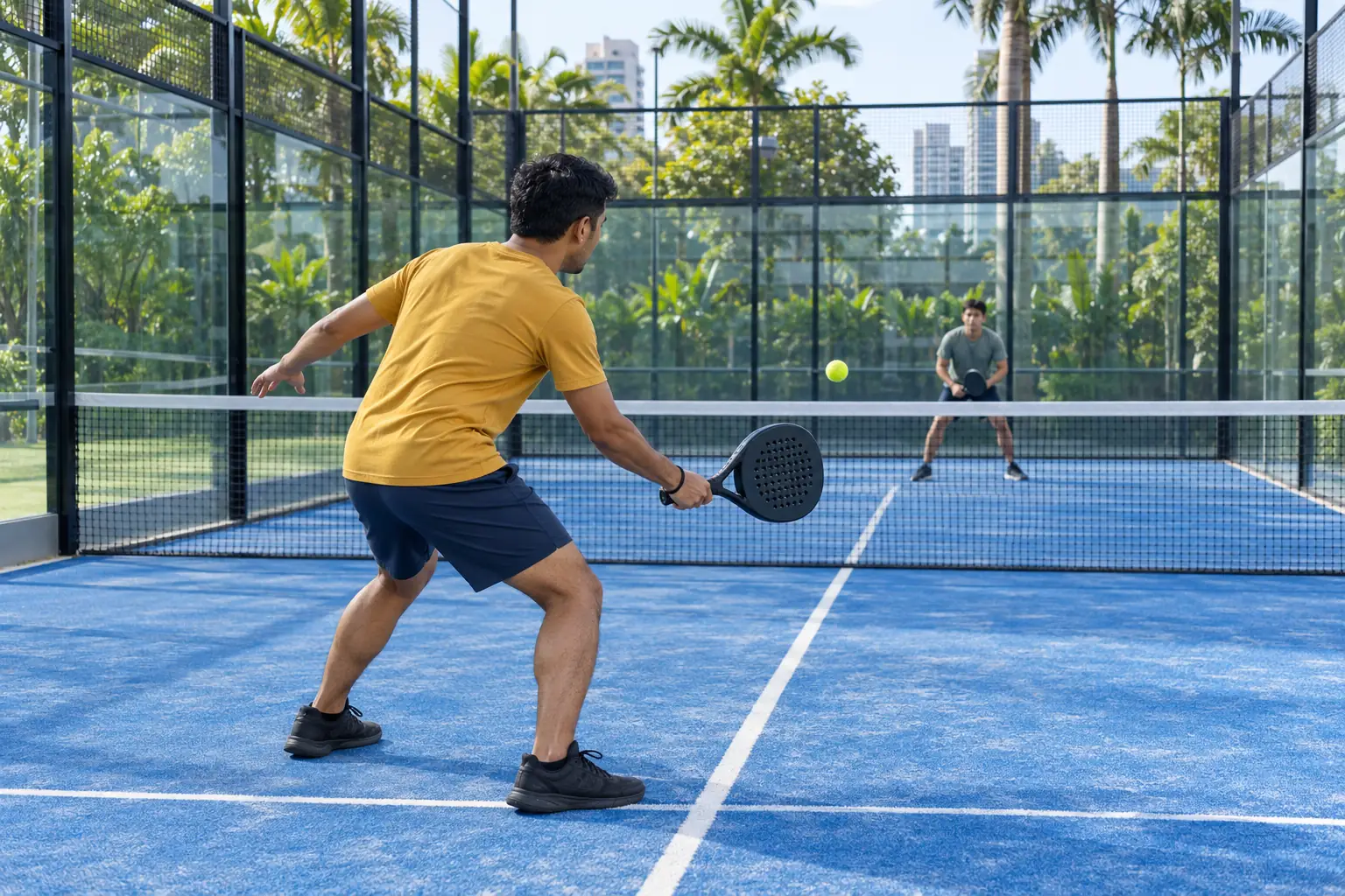 A Malay man prepares a forehand on his own side of a padel court facing the net.