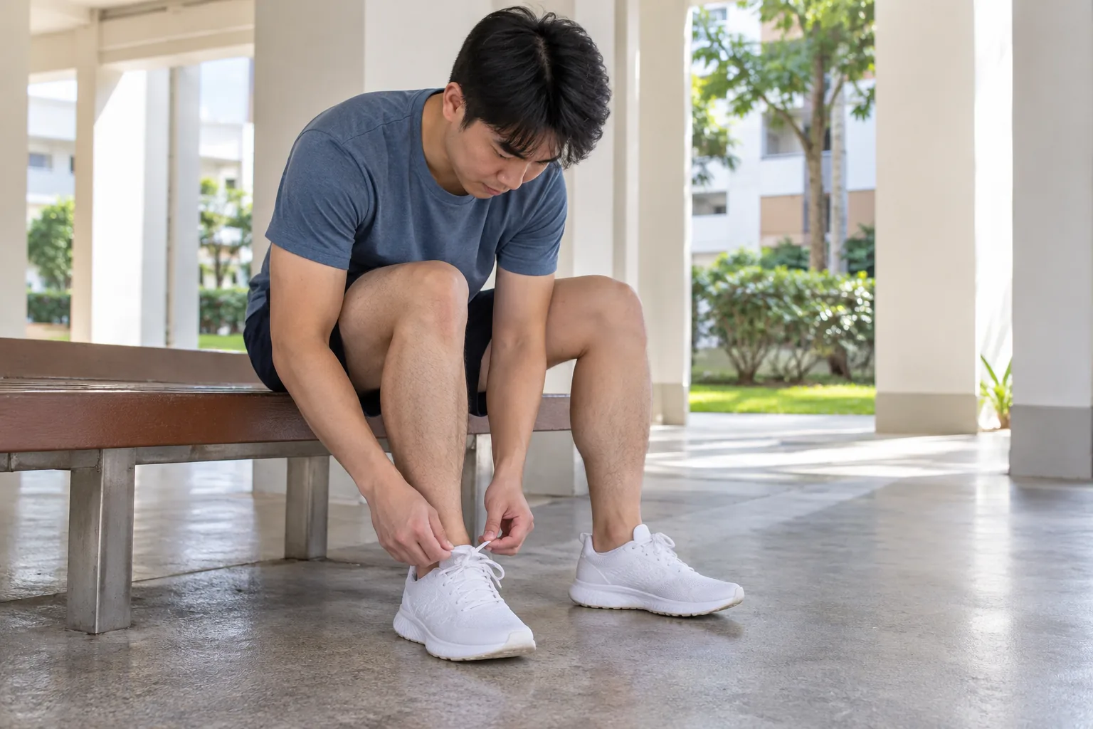A young man sits beneath a housing block and unlaces one training shoe while his other foot rests flat.
