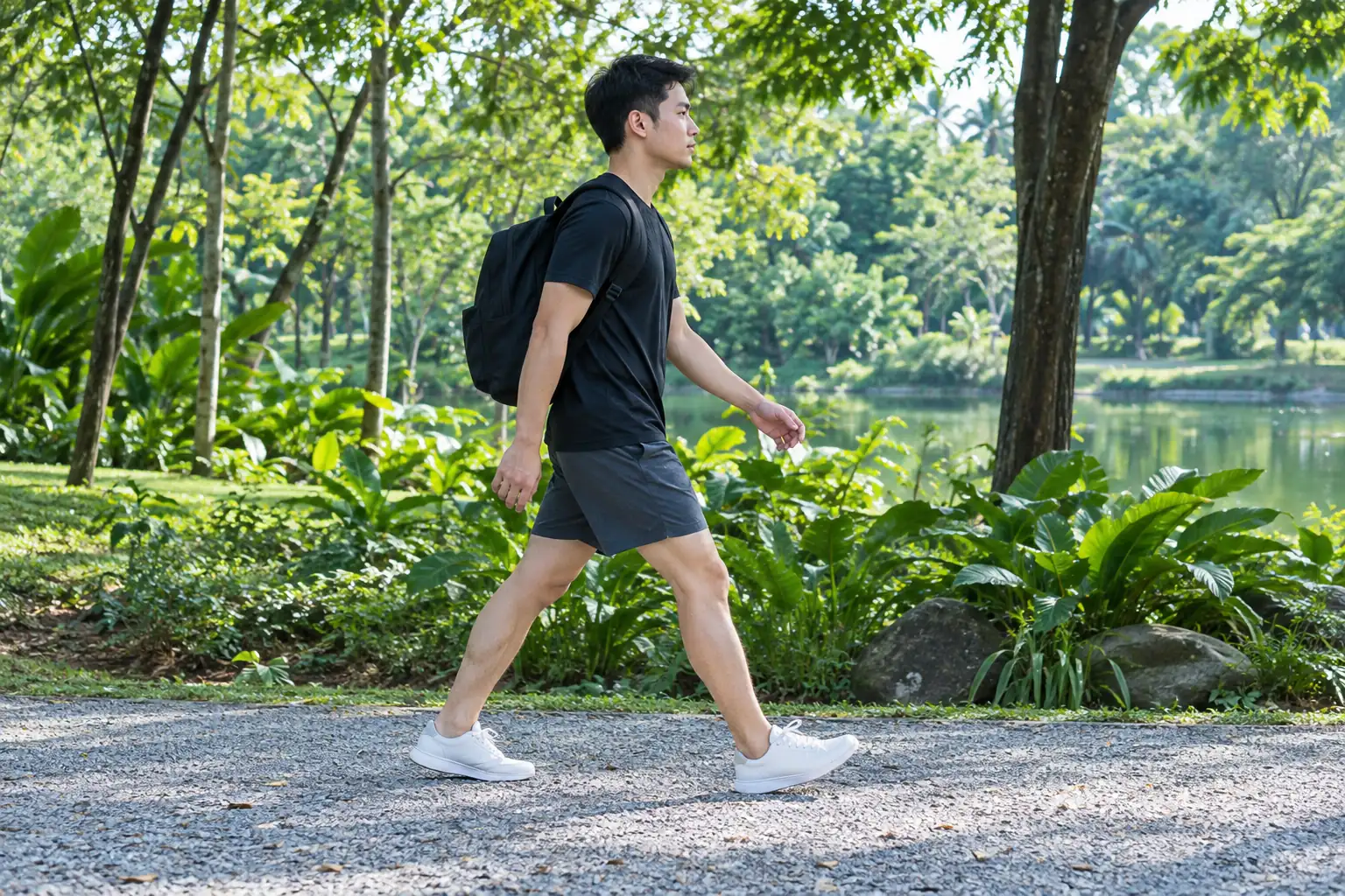 A young man with a backpack walks briskly along a gravel path with his knees and ankles visible.