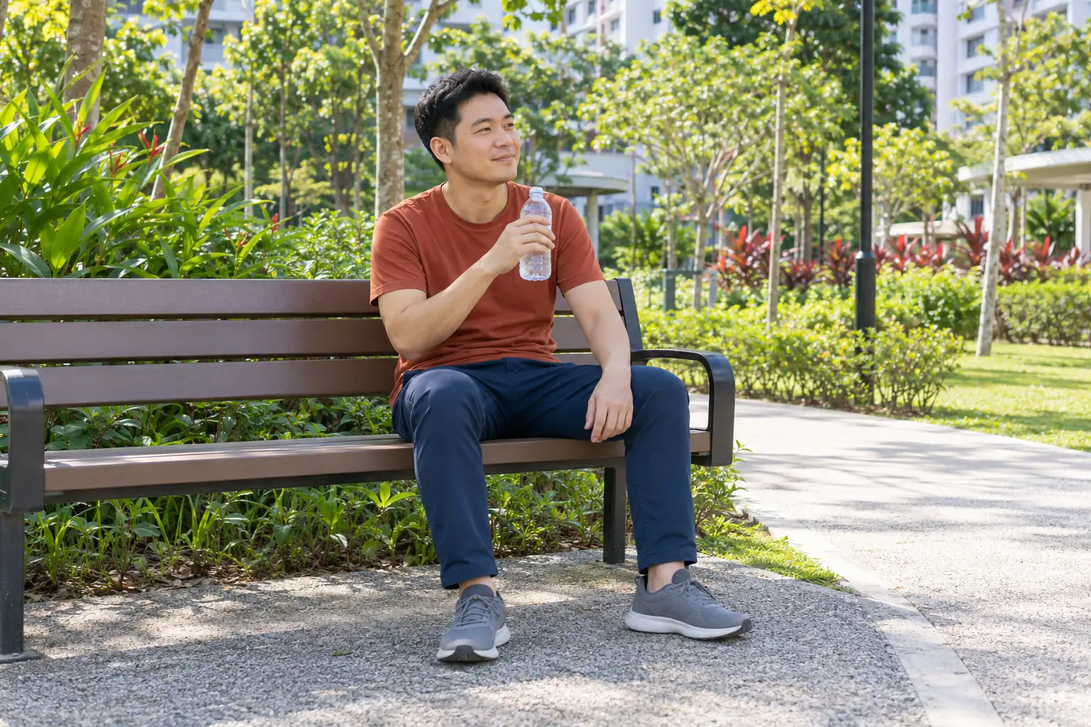 A Chinese man rests on a park bench with a bottle of water after a walk.