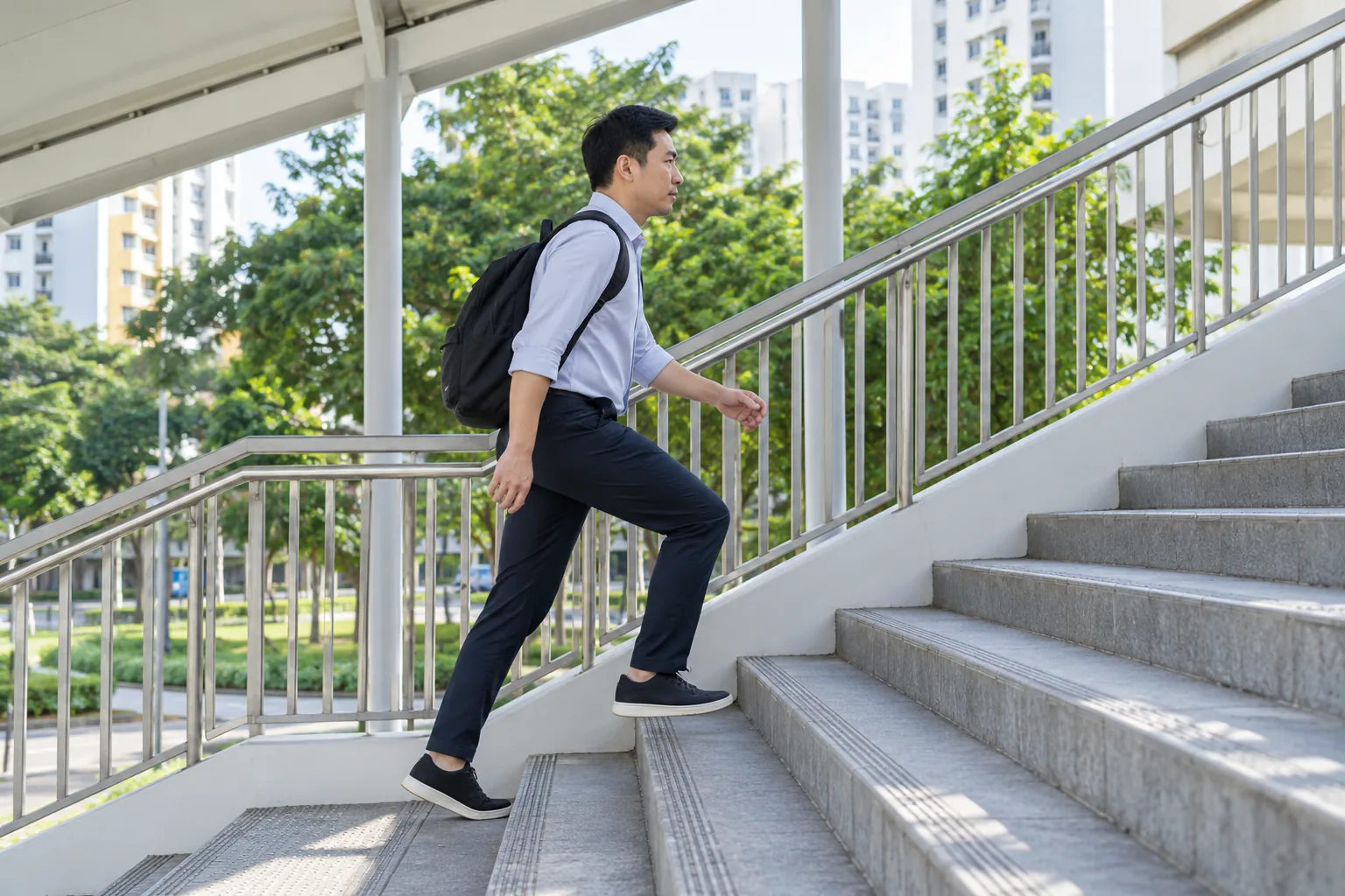 A man with a backpack walks briskly up the steps of a pedestrian bridge.