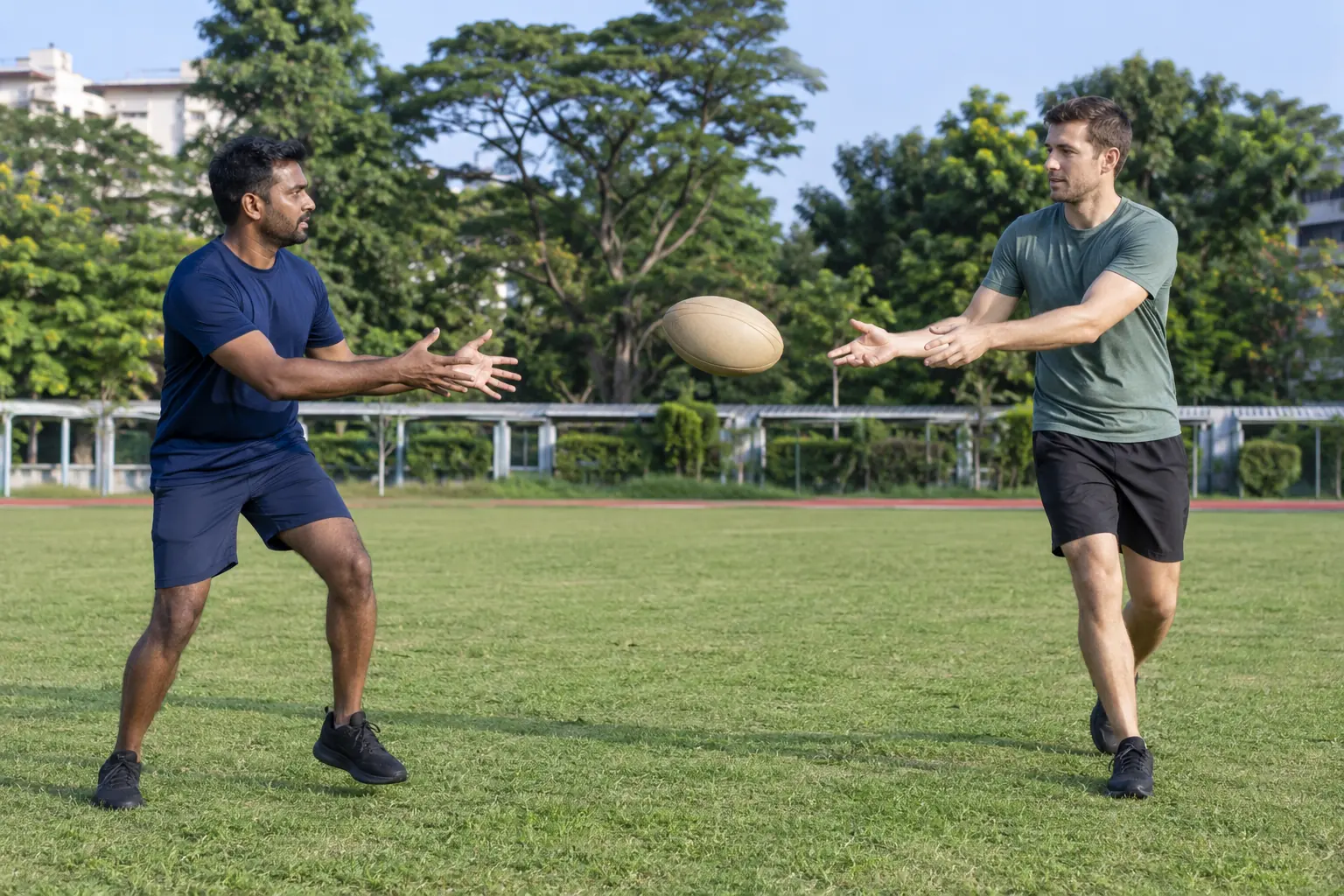 Two men pass a plain rugby ball on a Singapore grass field.